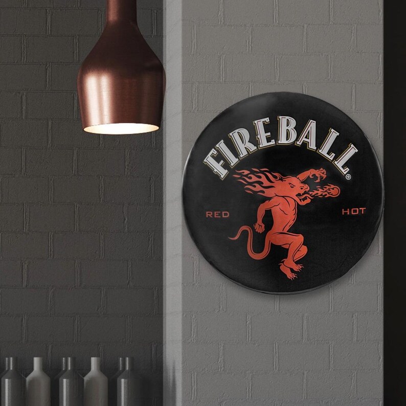 以下が含まれることがあります： 「Fireball Red Hot」の文字と、炎をまとった赤い悪魔のキャラクターが描かれた、黒と赤の丸い金属製の看板です。