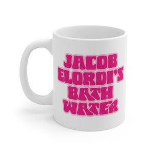 May include: White ceramic mug with a pink design that says "Jacob Elordi's Bath Water".