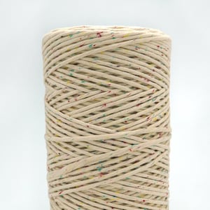 May include: A spool of natural coloured cotton cord with multi-coloured speckles. The cord is wound tightly around a cardboard tube.