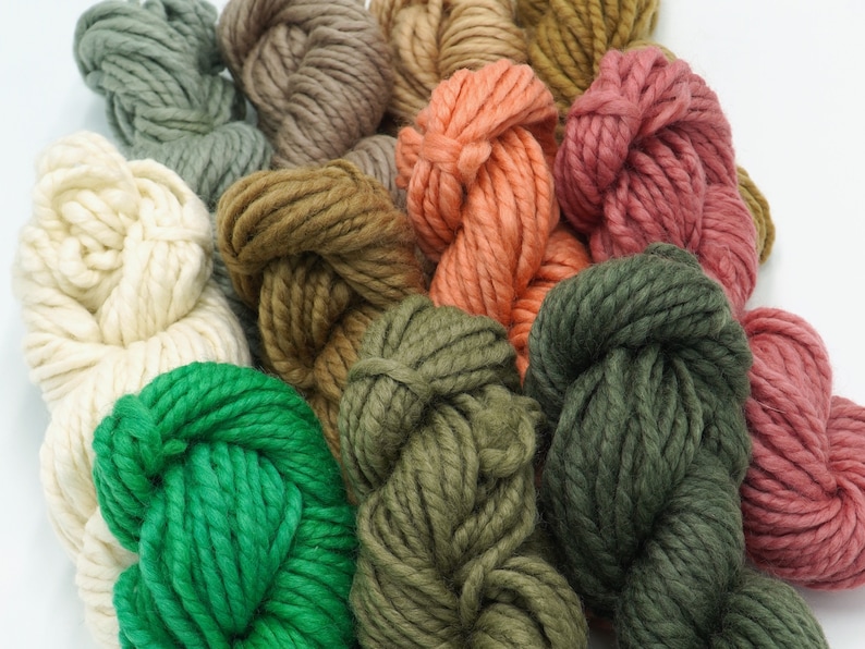 May include: A collection of yarn skeins in various shades of green, brown, cream, pink, and red. The yarn is arranged in a circular pattern, with the ends of the skeins overlapping.
