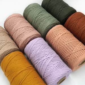 May include: Six spools of cotton rope in various colours, including beige, light pink, lavender, mustard yellow, forest green, and burnt orange. The rope is thick and has a braided texture.