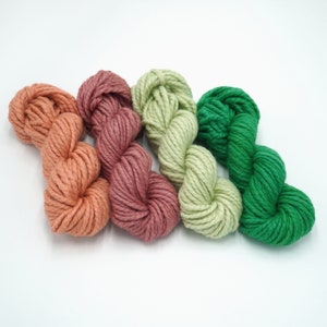 May include: Three skeins of yarn in shades of peach, light green, and forest green. The yarn is soft and fluffy, perfect for knitting or crocheting.