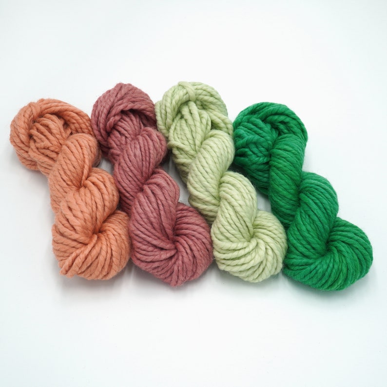 May include: Three skeins of yarn in shades of peach, light green, and forest green. The yarn is soft and fluffy, perfect for knitting or crocheting.