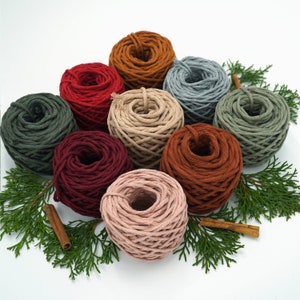 May include: Assortment of eight spools of colourful cotton rope, arranged in a circle on a white background with green sprigs of foliage. The rope is a natural fibre and has a rustic, handmade look.