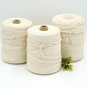 May include: Three spools of natural cotton rope, each wound around a cardboard core. The rope is a creamy white colour and has a slightly textured surface.