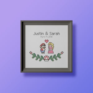 May include: A framed cross-stitch design featuring the video game characters Mario and Princess Peach. The text "Justin & Sarah April 14, 2018" is above the characters.