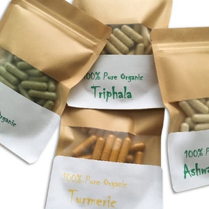 Puede incluir: Cuatro bolsas de papel marr&oacute;n con etiquetas blancas. Cada bolsa contiene c&aacute;psulas y tiene una etiqueta con el texto "100% Pure Organic" y el nombre de una hierba: Neem, Triphala, C&uacute;rcuma y Ashwagandha.