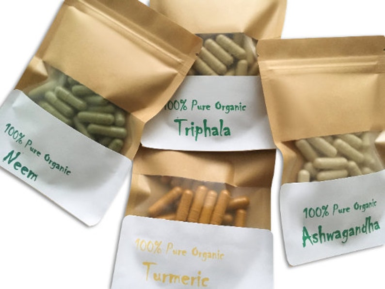Puede incluir: Cuatro bolsas de papel marr&oacute;n con etiquetas blancas. Cada bolsa contiene c&aacute;psulas y tiene una etiqueta con el texto "100% Pure Organic" y el nombre de una hierba: Neem, Triphala, C&uacute;rcuma y Ashwagandha.