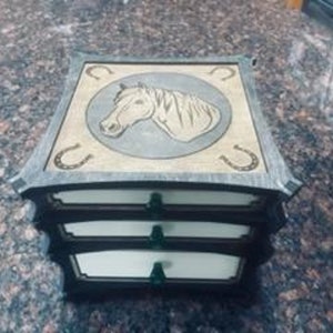 May include: A wooden box with three drawers, featuring a horse head design on the top. The box is decorated with horseshoe accents and has a rustic, distressed finish.