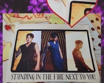 May include: A white canvas zippered pouch with three photos of men in black and blue clothing. The pouch has the text "Standing in the Fire Next to You" printed on the bottom.
