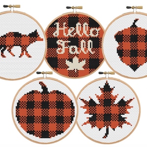 May include: Five embroidery hoops with different fall-themed designs. The designs include a fox, a pumpkin, a maple leaf, an acorn, and the words "Hello Fall". All designs are in a black and orange buffalo plaid pattern.