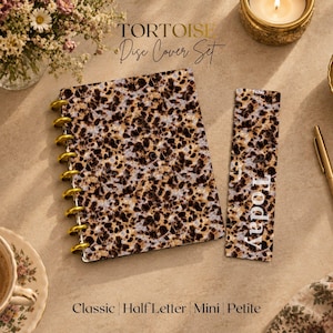 May include: A disc-bound notebook cover and a matching bookmark, both featuring a brown, black, and cream tortoise shell pattern. The notebook has gold-colored discs along the left side. The bookmark includes the white text Today.