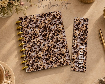 May include: A disc-bound notebook cover and a matching bookmark, both featuring a brown, black, and cream tortoise shell pattern. The notebook has gold-colored discs along the left side. The bookmark includes the white text Today.