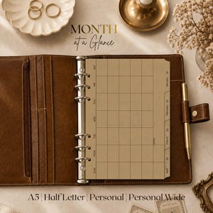 May include: A brown leather A5 binder open to a month at a glance calendar page with a grid layout, silver metal rings, and a gold pen attached to the side. The page features text reading Month at a Glance, January, February, March, and April.