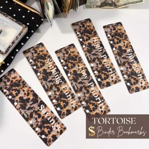 May include: Five rectangular plastic binder bookmarks featuring a brown and black tortoise shell pattern. Each bookmark has white text labels reading Savings, Sinking Funds, Low Priority, High Priority, and Emergency, with punched holes along the side.