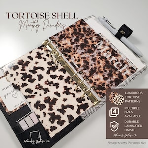 May include: A planner with tortoise shell patterned monthly dividers, featuring a gold six-ring binder mechanism. The page shows the text March. A white pen with a black clip is attached to the top. The planner has a black cover with pockets.