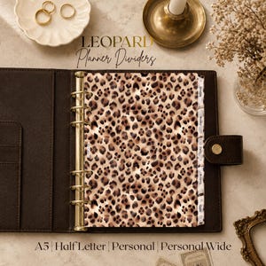 May include: A dark brown leather planner binder featuring a gold six-ring mechanism and leopard print dividers. The dividers include tabs labeled Monthly, Weekly, Daily, Projects, and Goals. The text LEOPARD Planner Dividers is visible.
