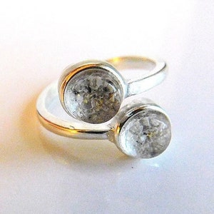 May include: A silver ring with two clear glass stones set in the band. The stones are round and have a speckled appearance.