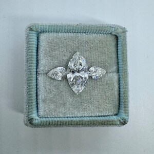 May include: A three-stone engagement ring with a large marquise-shaped center stone and two smaller pear-shaped side stones. The ring is set in a white metal band and is displayed in a blue velvet ring box.