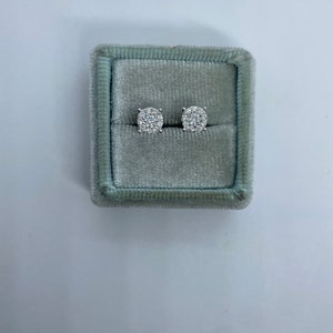 May include: A pair of silver stud earrings with a round cluster of small diamonds in a gray velvet jewelry box.
