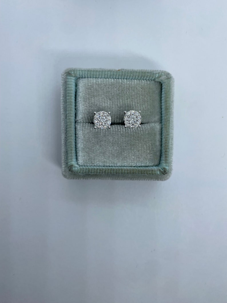 May include: A pair of silver stud earrings with a round cluster of small diamonds in a gray velvet jewelry box.
