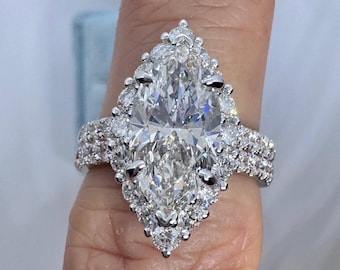 Puede incluir: Un deslumbrante anillo de compromiso con un gran diamante en forma de pera como pieza central. El diamante está rodeado de piedras más pequeñas y brillantes, engastadas en una banda de metal blanco. El diseño del anillo es intrincado y elegante.