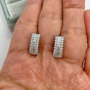 May include: A pair of silver hoop earrings with a row of baguette-shaped diamonds set in each hoop.
