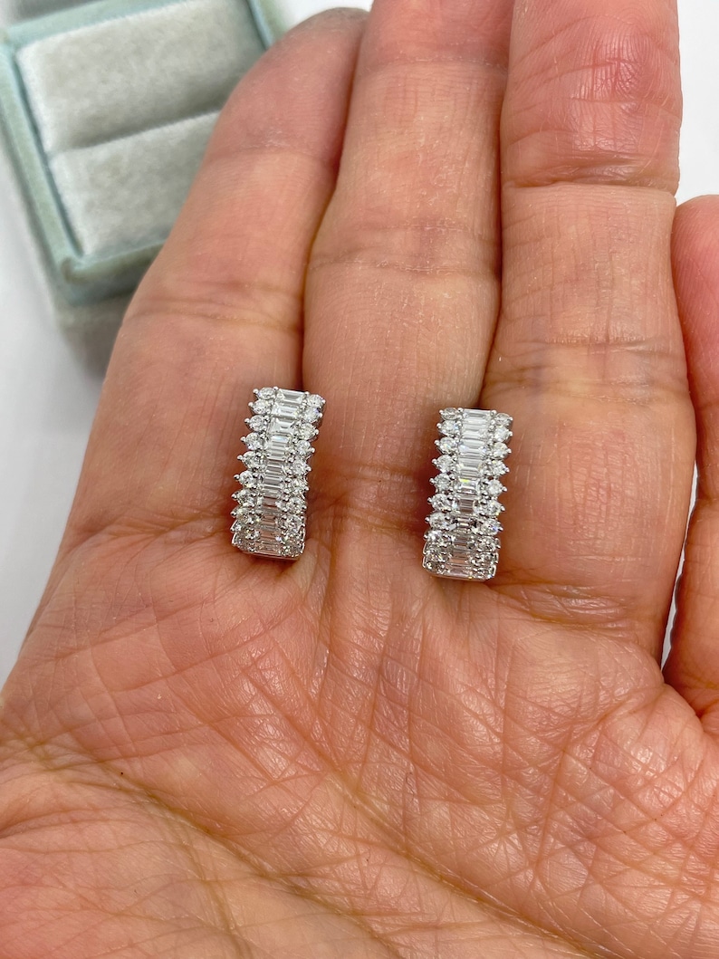 May include: A pair of silver hoop earrings with a row of baguette-shaped diamonds set in each hoop.