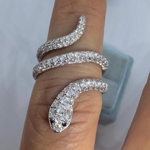May include: A silver snake ring, covered in many small, clear, sparkling stones. The snake coils around the finger, with the head at the tip and the tail curving around the top. The snake's eyes are black.