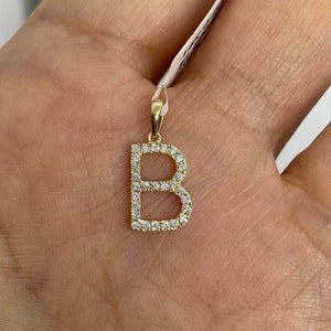 May include: A gold pendant charm in the shape of the letter B, with small clear diamonds set around the edges.