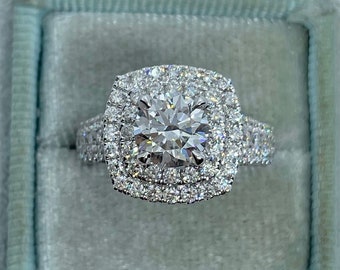 May include: A silver engagement ring with a large, round, center diamond surrounded by two rows of smaller diamonds.
