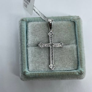 May include: A silver cross pendant with small clear stones set in the design. The pendant is in a light blue velvet box.