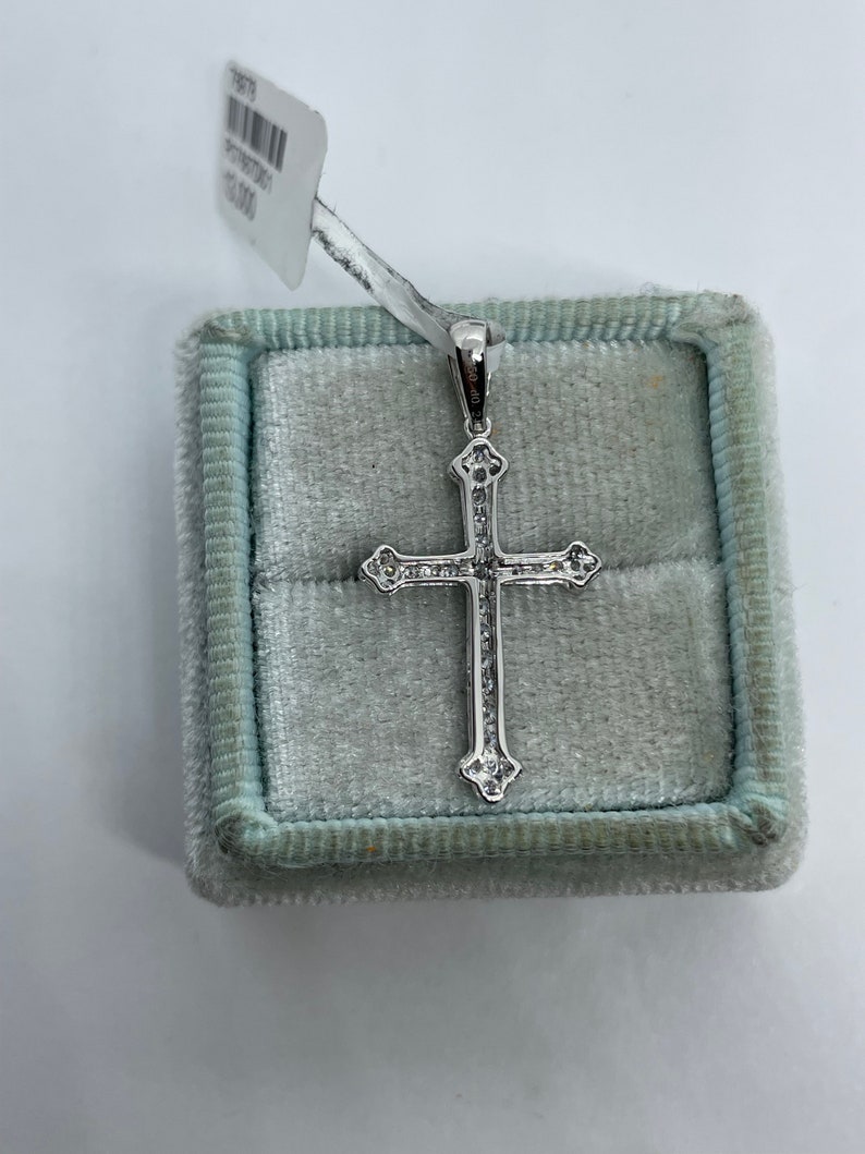 May include: A silver cross pendant with small clear stones set in the design. The pendant is in a light blue velvet box.