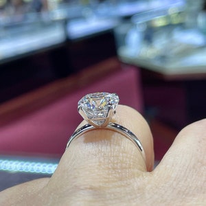 Puede incluir: Un anillo de compromiso de plata con un gran diamante redondo y claro.