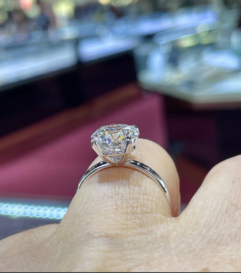 Puede incluir: Un anillo de compromiso de plata con un gran diamante redondo y claro.