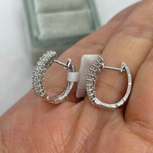 May include: A pair of silver hoop earrings with small diamonds set in the metal. The earrings are shown on a hand.