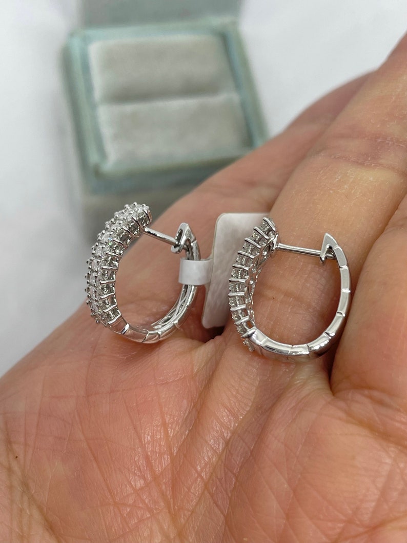 May include: A pair of silver hoop earrings with small diamonds set in the metal. The earrings are shown on a hand.