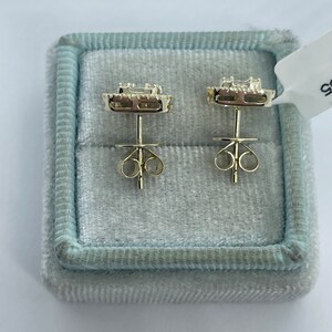 May include: A pair of gold earrings with a square-shaped diamond in the center surrounded by smaller diamonds. The earrings are in a blue velvet box.