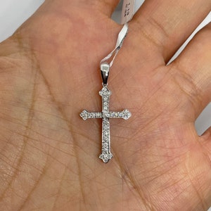 May include: A silver cross pendant with small diamonds set into the metal. The pendant is on a white string with a tag that reads "18K 0.113 0.13A".