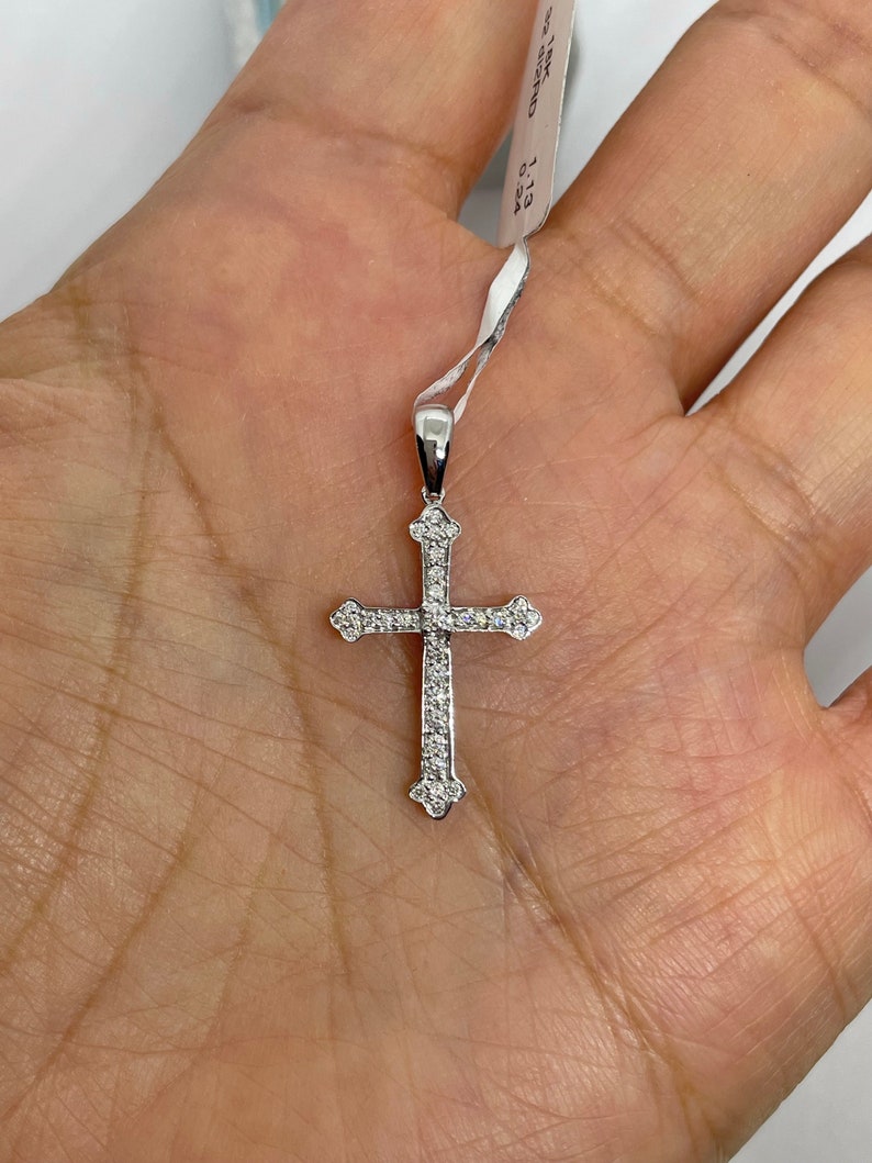 May include: A silver cross pendant with small diamonds set into the metal. The pendant is on a white string with a tag that reads "18K 0.113 0.13A".