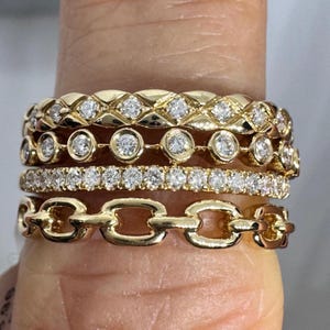 May include: Four gold rings with diamonds. The top ring has a woven design, the second ring has round diamonds, the third ring has small diamonds, and the bottom ring has a chain link design.