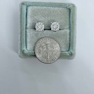 May include: A pair of diamond stud earrings in a blue velvet jewelry box next to a US dime coin.