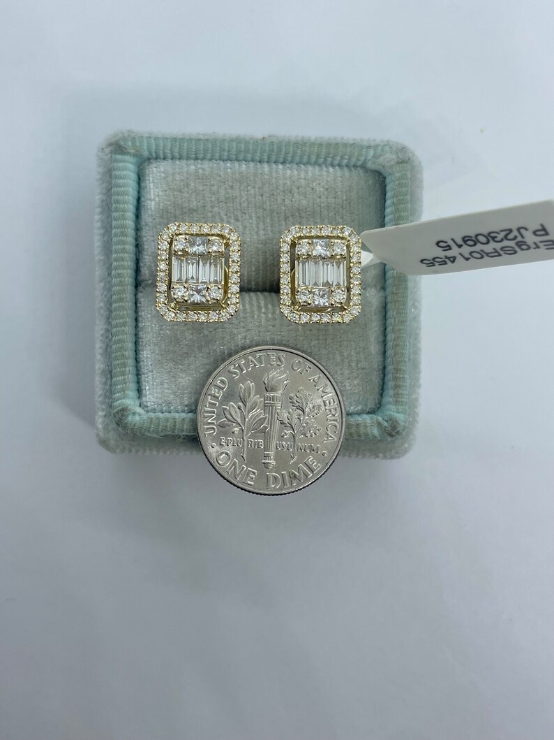 May include: A pair of gold earrings with a square shape and a row of baguette diamonds in the center. The earrings are in a blue velvet box with a dime for scale. The box has a label that reads "ET5P01A5S P 320615".