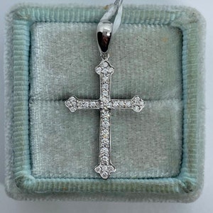 May include: A silver cross pendant with a white diamond encrusted design. The pendant is displayed in a blue velvet jewellery box.