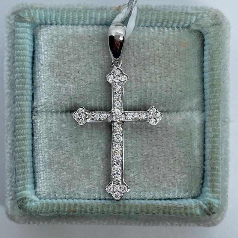 May include: A silver cross pendant with a white diamond encrusted design. The pendant is displayed in a blue velvet jewellery box.