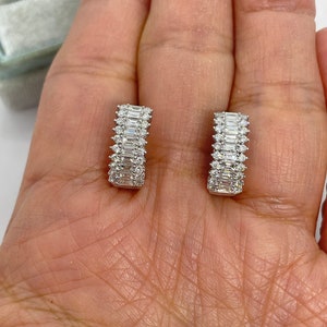 May include: A pair of silver hoop earrings with a row of baguette-shaped diamonds set in a channel setting.
