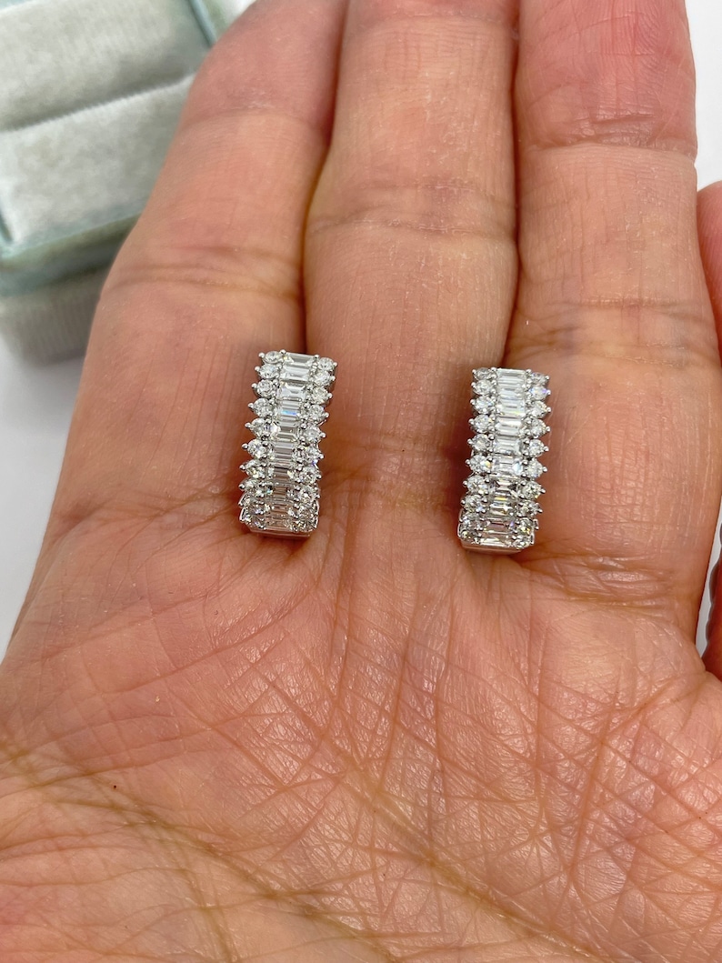 May include: A pair of silver hoop earrings with a row of baguette-shaped diamonds set in a channel setting.