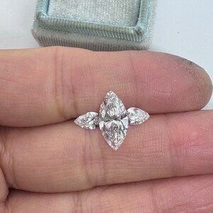 May include: A three-stone marquise diamond engagement ring with a large center stone and two smaller side stones.