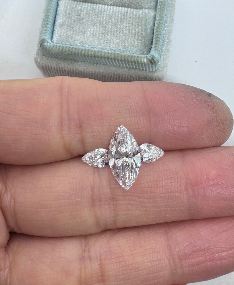 May include: A three-stone marquise diamond engagement ring with a large center stone and two smaller side stones.