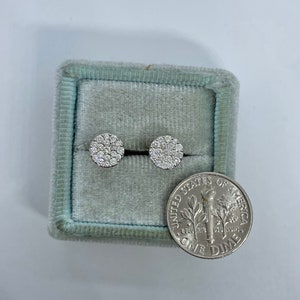 May include: A pair of round diamond earrings in a blue velvet jewelry box next to a US dime coin.